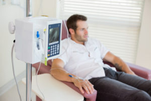 IV drip attached to young male patient's hand during chemotherapy in hospital room